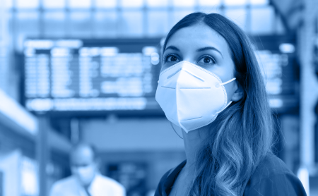 Woman with PPE face mask stands in a public place, blue wash over image