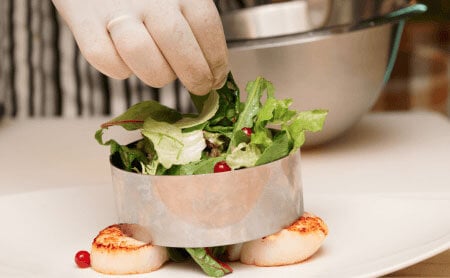 Gloved hand putting a salad garnish on scallops