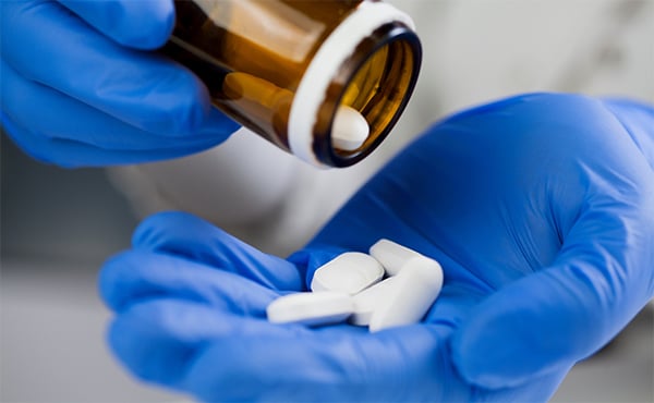 Close up of a medical professional's gloved hands. Using one hand to shake white, oval pills out of a brown glass bottle and into their other hand
