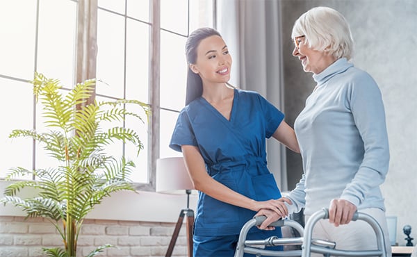 A nurse helps her patient, an older woman using a walker, during an office visit