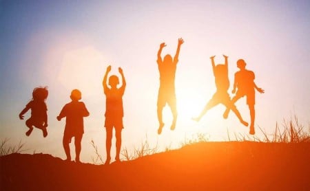 Silhouette of children jumping outside at sunset