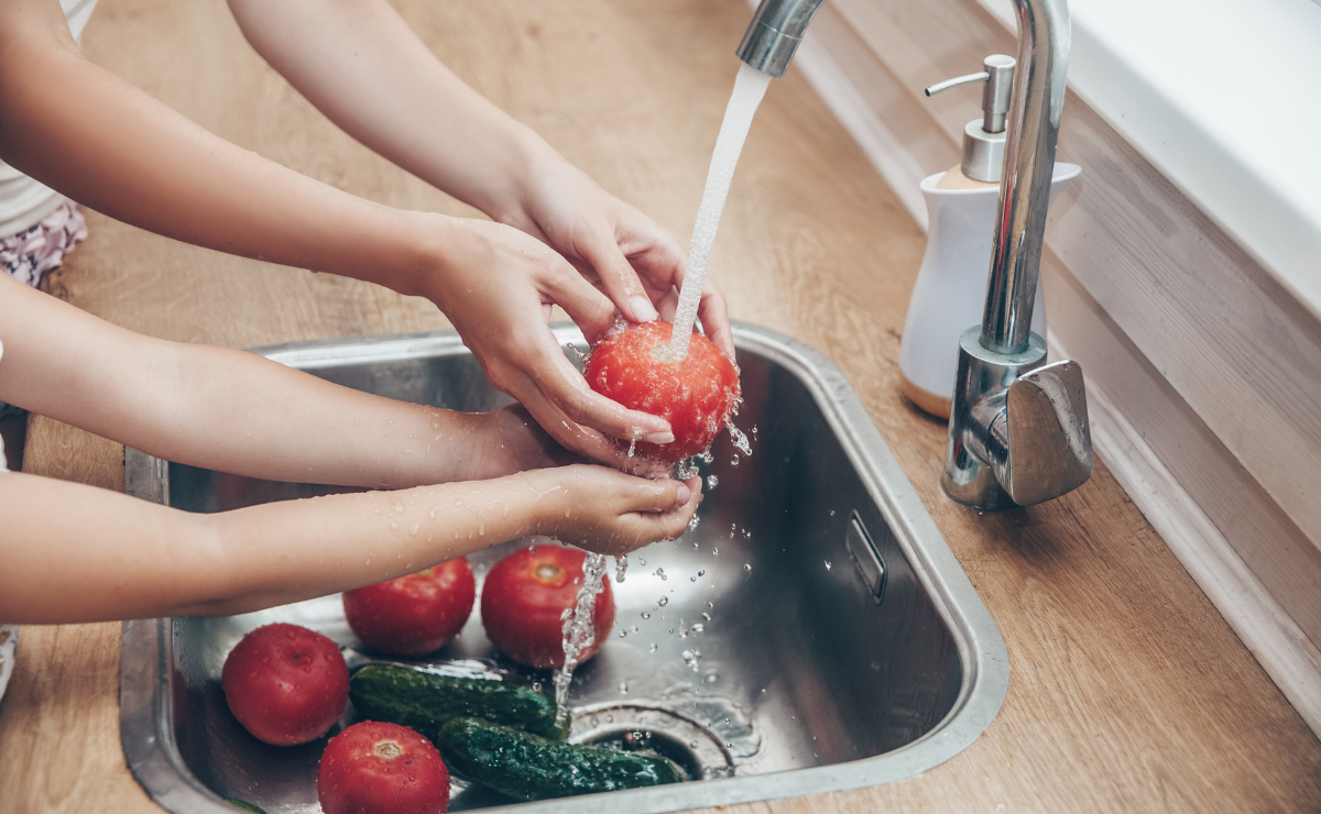 Two sets of hands washing fresh vegetables in a kitchen sink