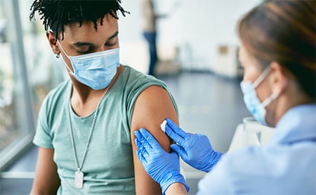 A nurse disinfects the spot on a young man's arm where she will give him a shot