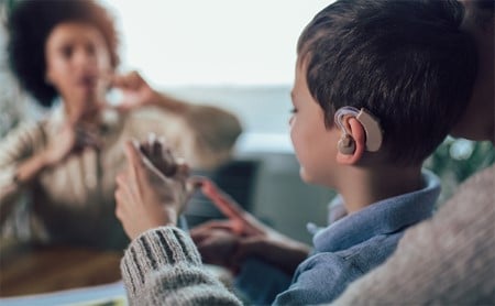 Young boy with a cochlear implant signing to an adult, who is signing back