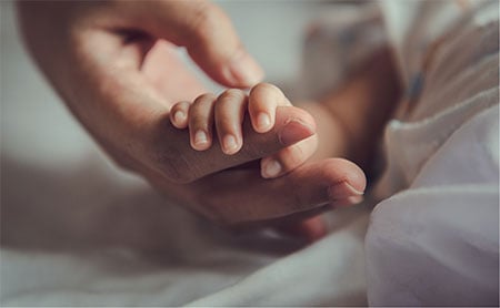Close-up of a small child’s hand gripping an adult’s finger.