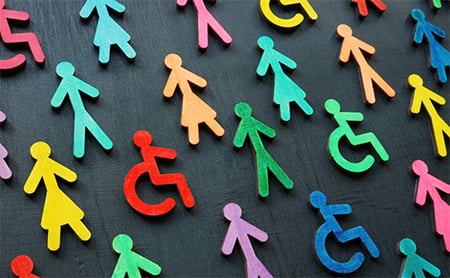 Colorful wooden stick figures, representing those with disabilities and those who are able-bodied, laid out on a dark grey background