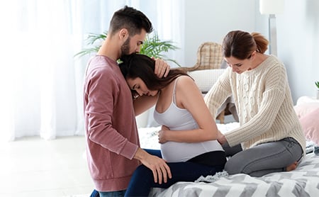 Couple comforting each other while pregnant woman receives maternal massage from her doula
