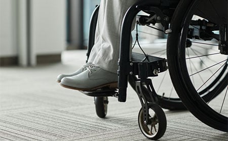Close-up of a person’s lower legs and feet resting on the footplate of a wheelchair.