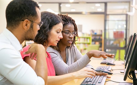 Three adults collaborate in a computer lab