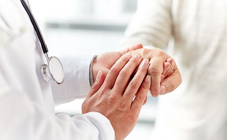 Closeup of doctor holding the hands of a patient, implying comfort.