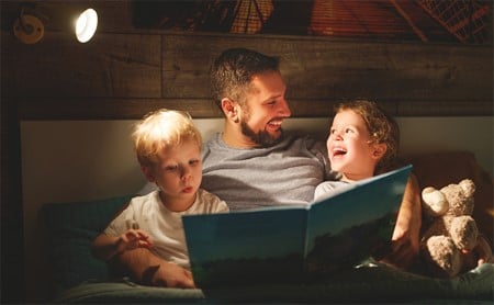 Smiling father reading bedtime story to two happy kids