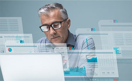 older man with glasses working at a computer and surrounded by digital files