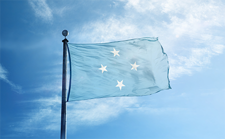 Flag of the Federated States of Micronesia waving in the wind with a blue sky in the background