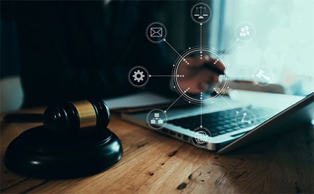 Person working on a laptop with a gavel and digital icons overlaid.