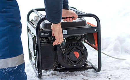 Close up of hands starting an outdoor generator with snow on the ground