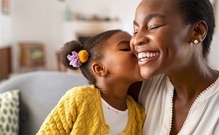 A young, happy Black girl kisses her mother on the cheek