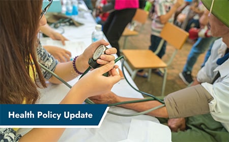 A community health worker takes someone's blood pressure reading at a community health clinic. ASTHO Health Policy Update banner in lower left