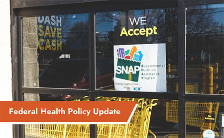 A grocery store window displays a sign reading “We Accept SNAP Supplemental Nutrition Assistance Program” with a caption below stating “Federal Health Policy Update.