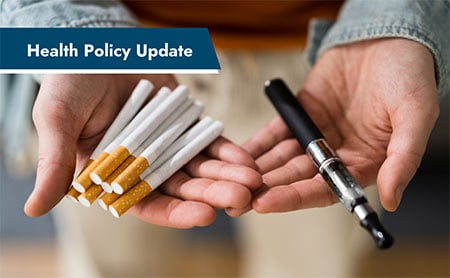 A pair of hands holding cigarettes and an electronic cigarette with the text ‘Health Policy Update’ above.