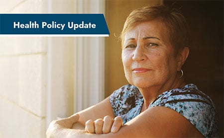 Woman in a blue patterned short-sleeved shirt sitting near a window with sunlight streaming in, the heading ‘Health Policy Update’ in the upper left corner.