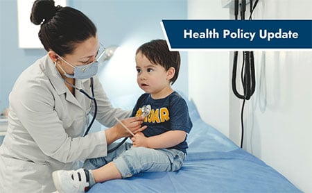 Masked pediatrician placing stethoscope on a little boy's chest in a doctors office