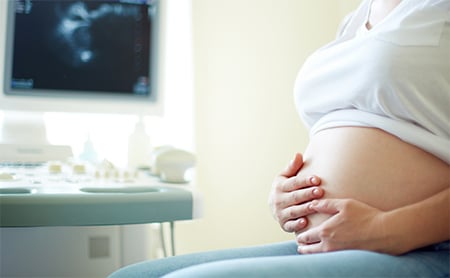 A pregnant person cradles their exposed belly in an exam room during an appointment
