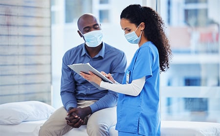A nurse and patient, both in PPE, talk during an appointment
