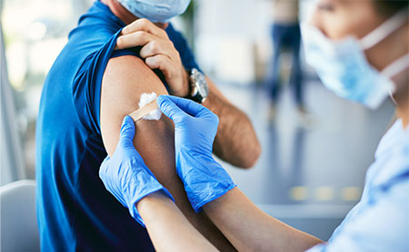 Close-up of nurse putting band-aid on man's arm after coronavirus vaccination.