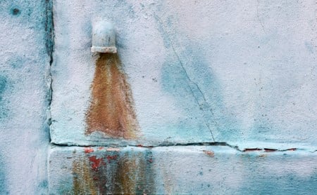 Outdoor drain pipe on a faded blue wall with a rusty trail stain from the water
