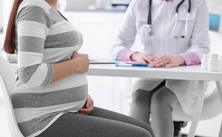 A pregnant woman sitting across the desk from her doctor during an office visit