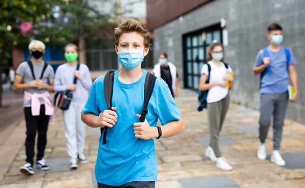 Teenager in protective face mask with backpack going to school on sunny day.