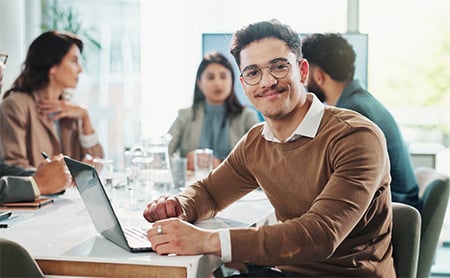 Young man working on a laptop at a confrence table with his coworkers